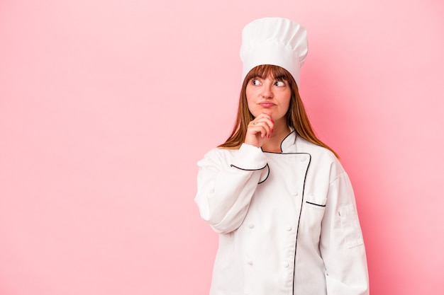 Mujer joven chef caucásica aislada sobre fondo rosa mirando hacia los lados con expresión dudosa y escéptica.