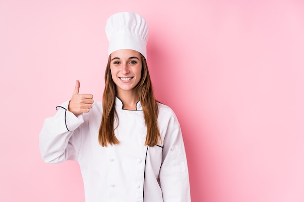 Mujer joven chef caucásico aislado sonriendo y levantando el pulgar hacia arriba