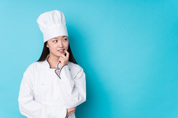 Mujer joven chef chino aislado relajado pensando en algo mirando un espacio de copia.