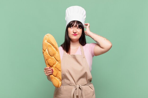 Mujer joven chef que se siente perpleja y confundida, rascándose la cabeza y mirando hacia un lado