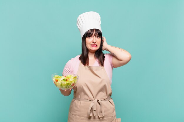 Mujer joven chef sintiéndose estresada, preocupada, ansiosa o asustada, con las manos en la cabeza, presa del pánico por el error