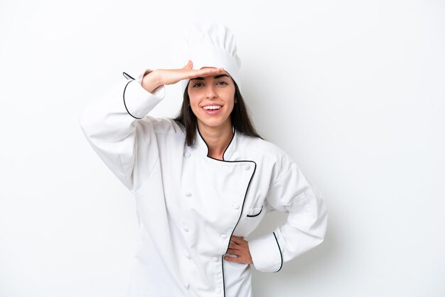 Mujer joven chef sobre fondo blanco mirando lejos con la mano para mirar algo