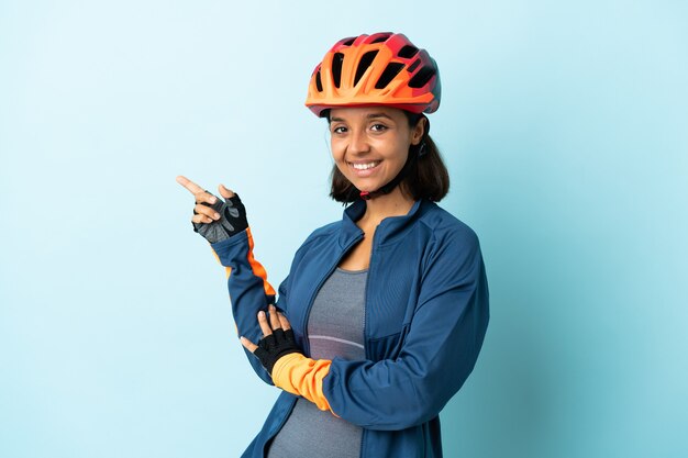 Foto mujer joven ciclista aislada en azul dedo acusador hacia el lado