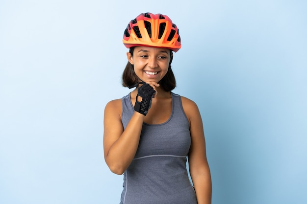 Mujer joven ciclista aislada en azul mirando hacia el lado y sonriendo