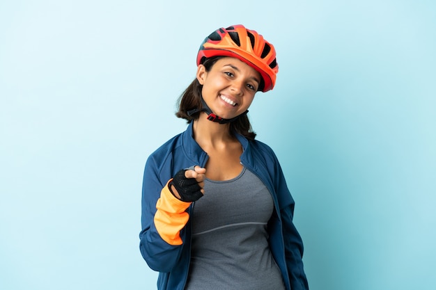 Mujer joven ciclista aislada en la pared azul apuntando al frente con expresión feliz