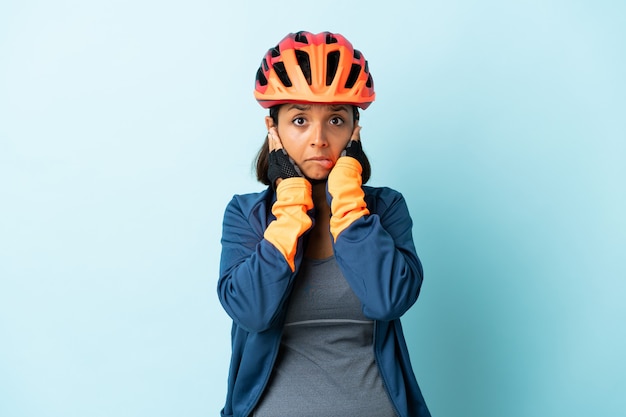 Mujer joven ciclista aislada en la pared azul frustrada y cubriendo las orejas