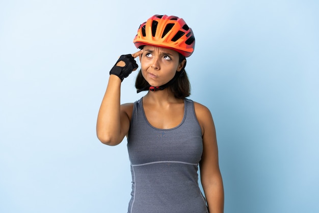 Mujer joven ciclista aislada en la pared azul haciendo el gesto de locura poniendo el dedo en la cabeza