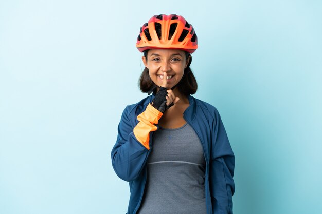 Mujer joven ciclista aislada en la pared azul que muestra un signo de gesto de silencio poniendo el dedo en la boca