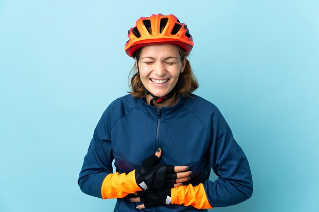 Mujer joven ciclista aislada en la pared azul sonriendo mucho