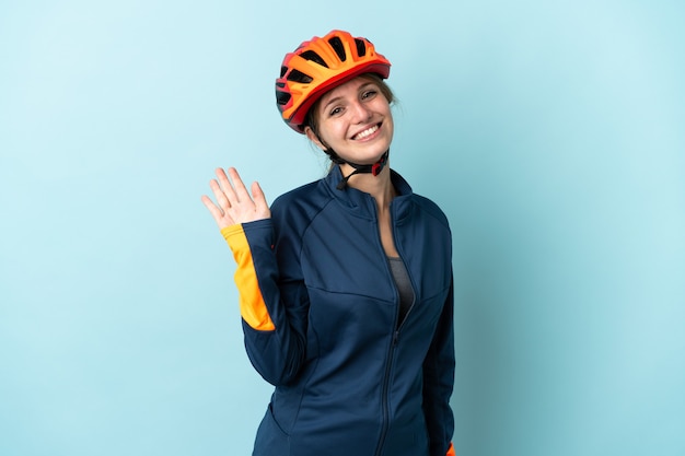 Mujer joven ciclista en azul saludando con la mano con expresión feliz