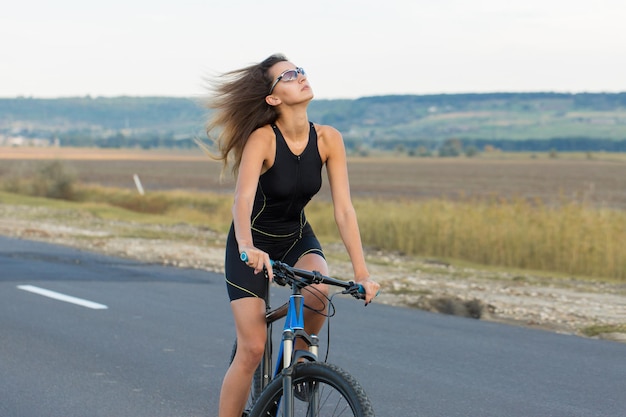 Mujer joven ciclista en bicicleta en la vista lateral de la carretera rural