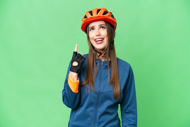 Mujer joven ciclista sobre fondo clave de croma aislado apuntando hacia arriba y sorprendida