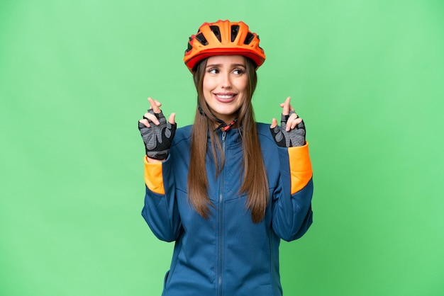 Mujer joven ciclista sobre fondo clave de croma aislado con los dedos cruzados