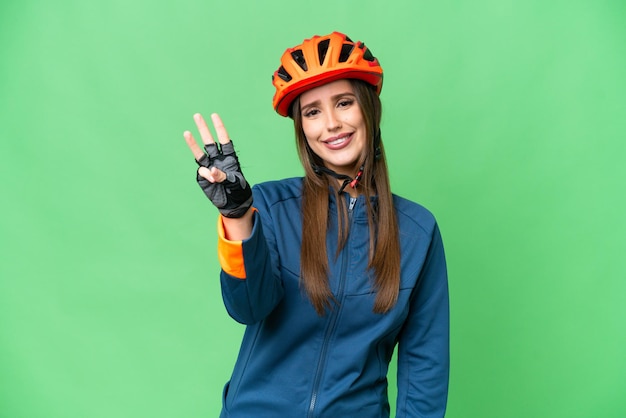 Mujer joven ciclista sobre fondo clave de croma aislado feliz y contando tres con los dedos