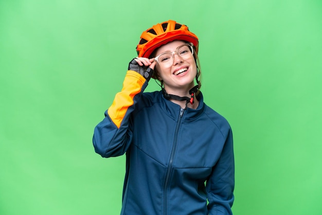 Mujer joven ciclista sobre fondo clave de croma aislado con gafas y feliz