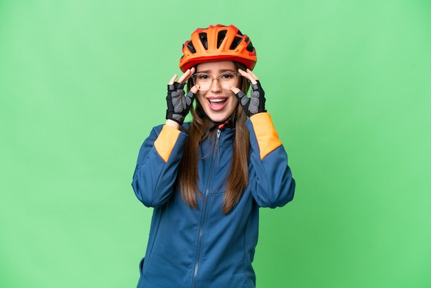 Mujer joven ciclista sobre fondo clave de croma aislado con gafas y sorprendido