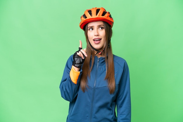 Mujer joven ciclista sobre un fondo clave de croma aislado pensando en una idea apuntando con el dedo hacia arriba