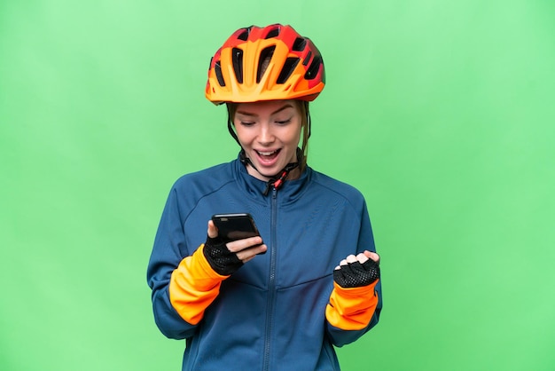 Mujer joven ciclista sobre fondo clave de croma aislado sorprendida y enviando un mensaje