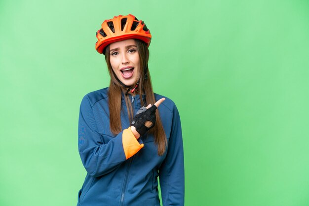 Mujer joven ciclista sobre fondo clave de croma aislado sorprendido y apuntando hacia el lado