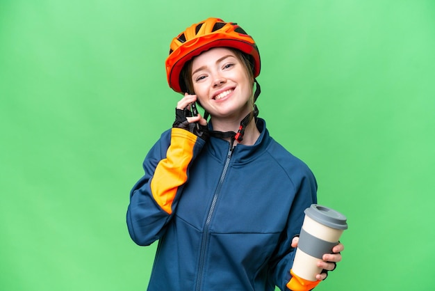 Mujer joven ciclista sobre fondo clave de croma aislado sosteniendo café para llevar y un móvil