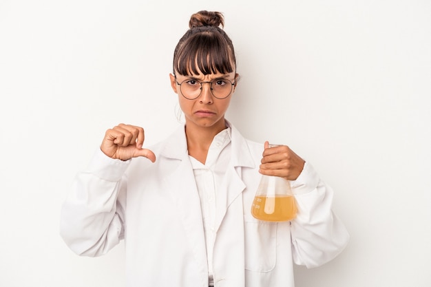 Mujer joven científico de raza mixta sosteniendo un tubo de ensayo aislado sobre fondo blanco mostrando un gesto de aversión, pulgares hacia abajo. Concepto de desacuerdo.