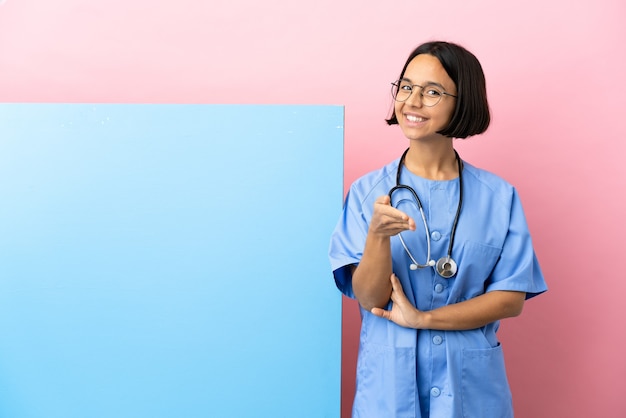 Mujer joven cirujano de raza mixta con una gran pancarta sobre fondo aislado un apretón de manos para cerrar un buen trato
