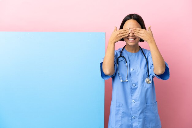 Mujer joven cirujano de raza mixta con una gran pancarta sobre fondo aislado cubriendo los ojos con las manos y sonriendo