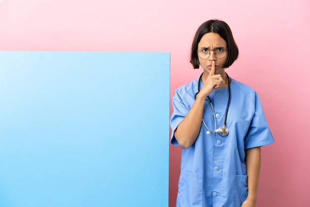 Mujer joven cirujano de raza mixta con una gran pancarta sobre fondo aislado que muestra una señal de gesto de silencio poniendo el dedo en la boca