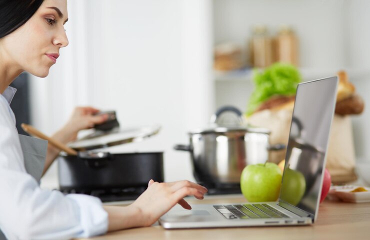 Foto mujer joven, en, cocina, con, computadora de computadora portátil, mirar, recetas, sonriente, comida, blogger, concepto