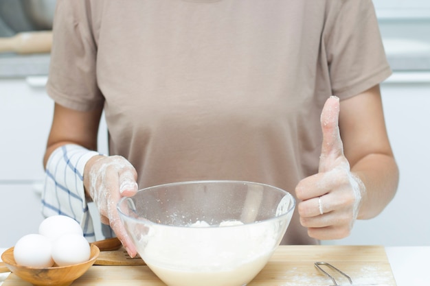 Una mujer joven en una cocina moderna sostiene una taza de harina y muestra su pulgar