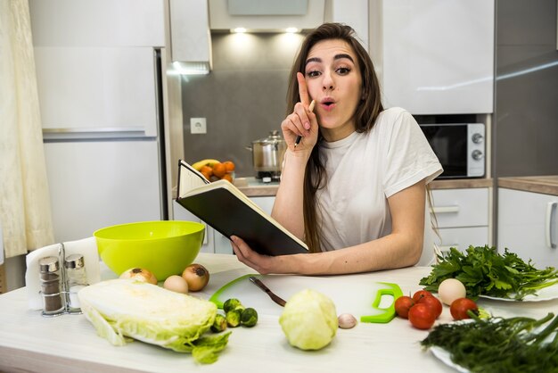 Mujer joven cocinando alimentos usando un bloc de notas como ayuda en su cocina.