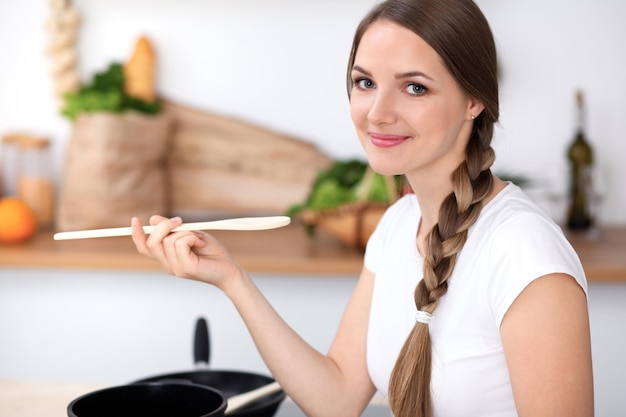 Foto la mujer joven está cocinando en una cocina el ama de casa está probando la sopa con una cuchara de madera