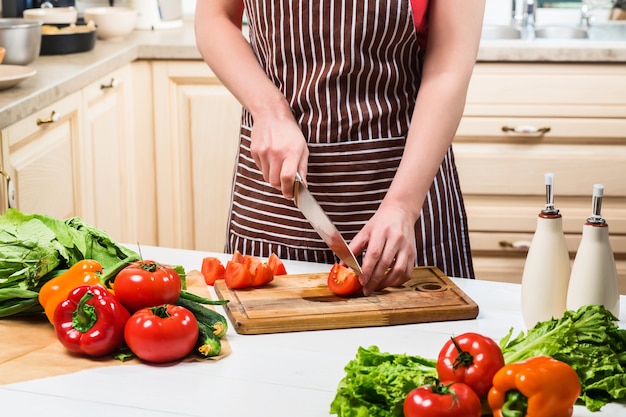 Mujer joven cocinando en la cocina de su casa. Comida sana. Dieta. Concepto de dieta. Estilo de vida saludable. Cocinar en casa. Prepara comida. Una mujer corta un tomate y verduras con un cuchillo.