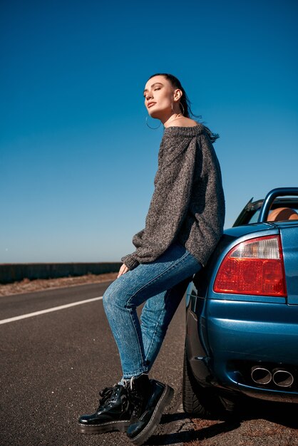 Mujer joven con una cola de pie cerca del coche sin techo al aire libre