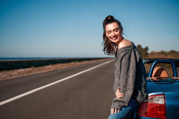 Mujer joven con una cola de pie cerca del coche sin techo al aire libre