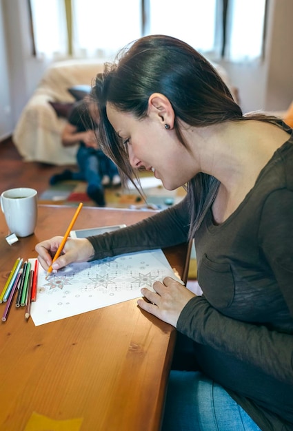 Mujer joven coloreando mandalas mientras toma un té en la sala Centrarse en la mujer en primer plano