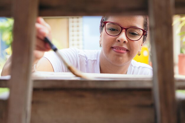 Mujer joven coloreando una silla vieja y divirtiéndose en casa.