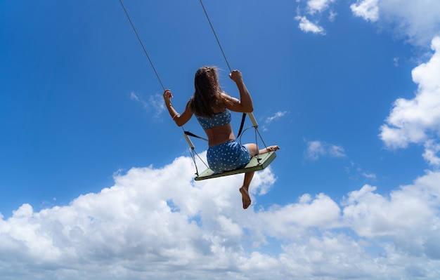 Mujer joven en el columpio con fondo de cielo azul. Concepto de libertad y felicidad. Foto de alta calidad