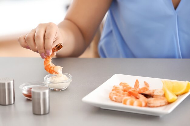 Mujer joven comiendo camarones en la mesa