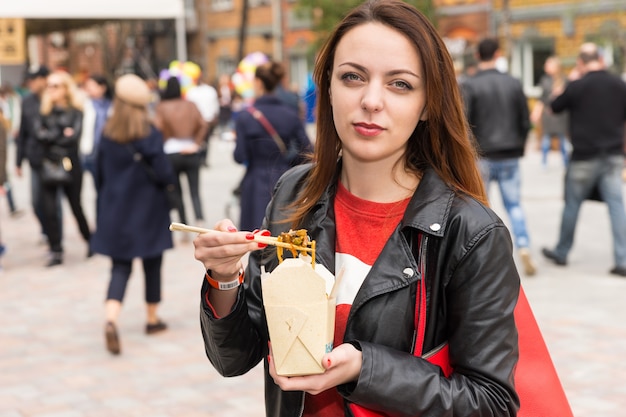 Mujer joven comiendo comida asiática para llevar en el concurrido Festival