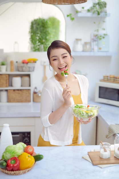 Mujer joven comiendo ensalada y sosteniendo una ensalada mixta.