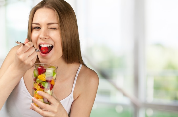 Foto mujer joven comiendo frutas de vidrio sobre fondo borroso