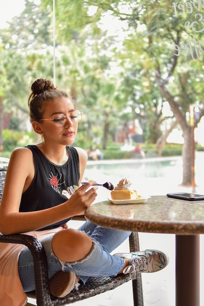 Foto mujer joven comiendo postre en una mesa en un café contra los árboles