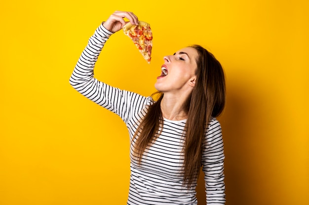 Mujer joven comiendo una rebanada de pizza fresca caliente en un amarillo.