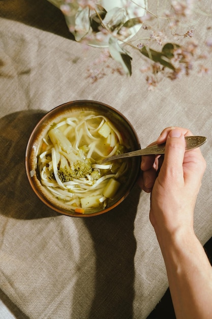 Mujer joven comiendo sopa de verduras con brócoli y fideos