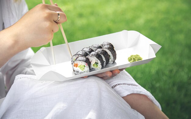 Una mujer joven comiendo sushi en la naturaleza maki roll closeup