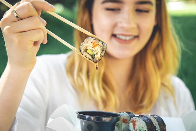 Una mujer joven comiendo sushi en la naturaleza maki roll closeup