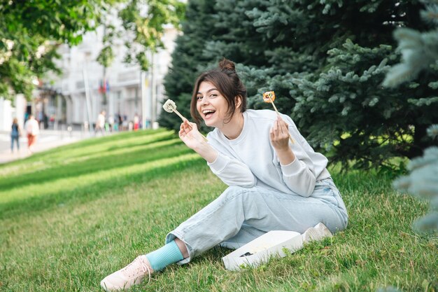 Una mujer joven comiendo sushi en el picnic del parque en la naturaleza