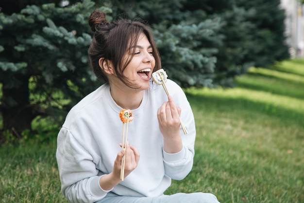 Una mujer joven comiendo sushi en el picnic del parque en la naturaleza