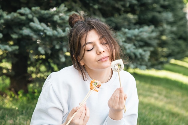 Una mujer joven comiendo sushi en el picnic del parque en la naturaleza